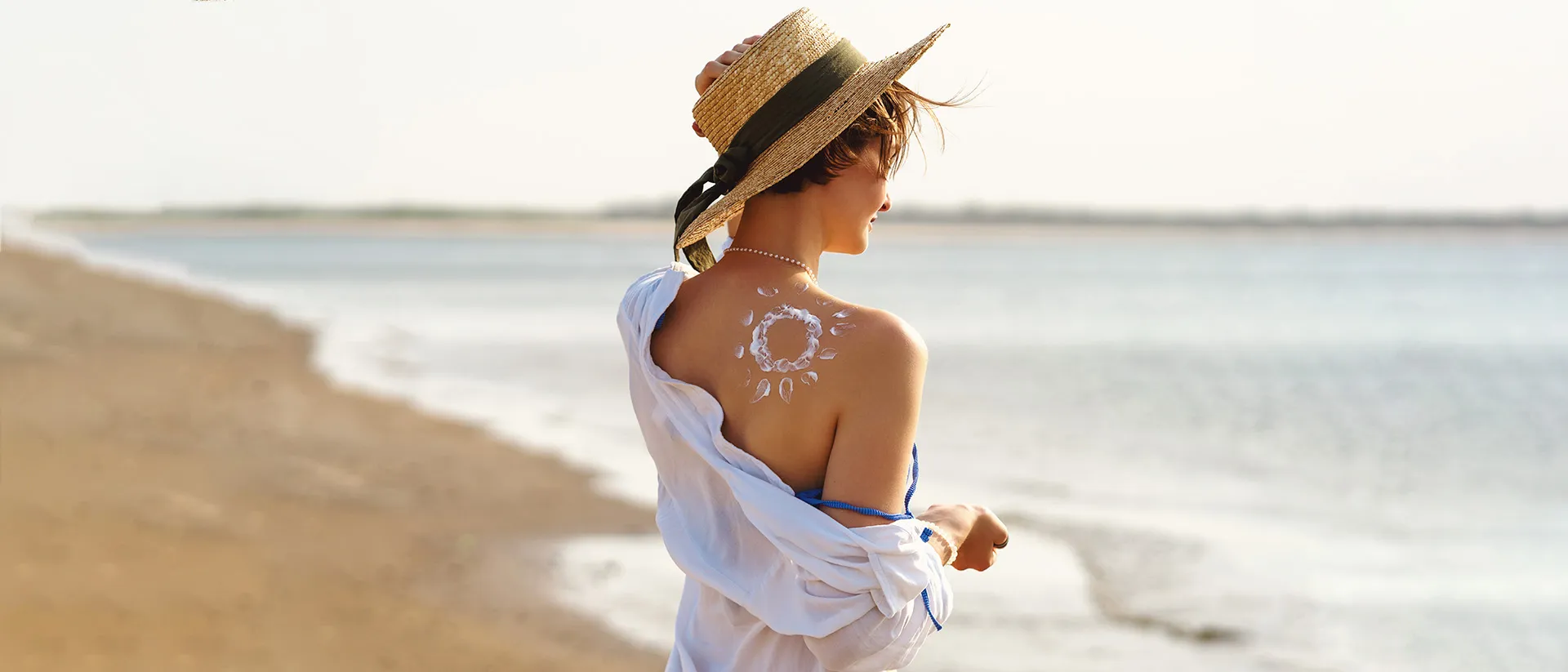 Woman at the beach with a sun drawn in sunscreen on her back, highlighting how often to reapply sunscreen.
