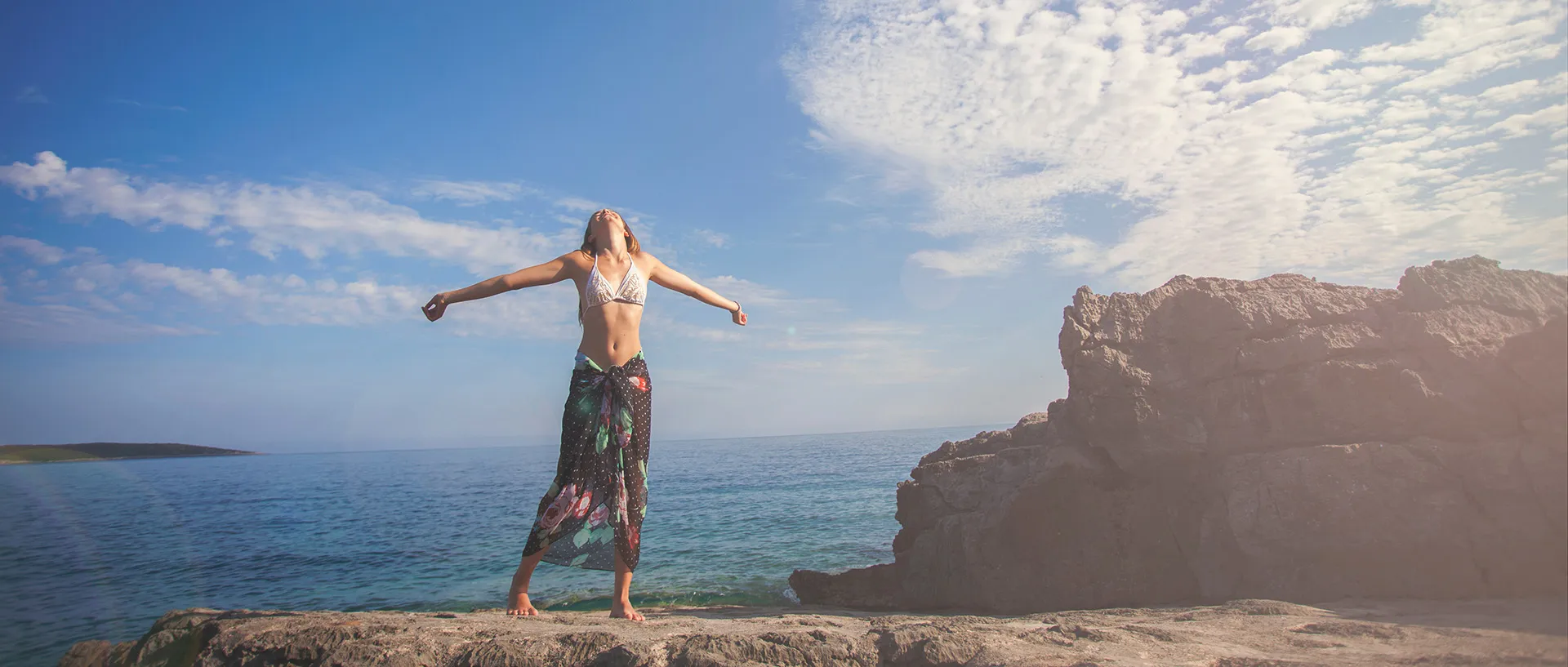 Woman enjoying sunshine by the sea, demonstrating sunscreen anti-aging benefits
