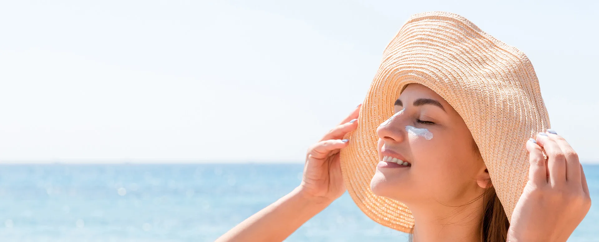 Woman at the beach with sun hat and sunscreen anti-aging care