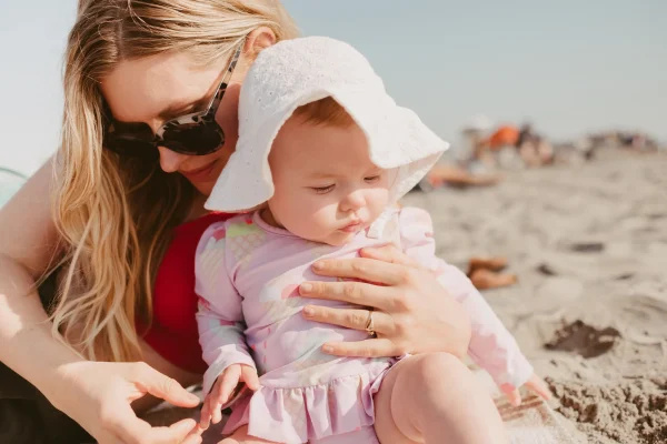 Mother applies sun protection for babies at the beach with a sun hat and long-sleeved clothing.